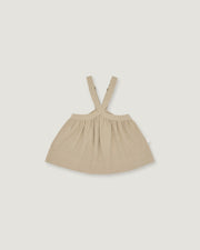 A light beige baby dress with shoulder straps, laid flat against a solid light gray background.