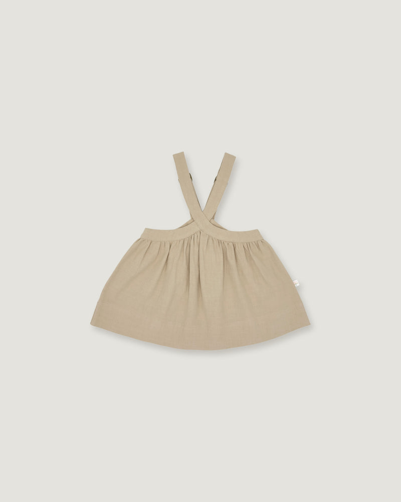 A light beige baby dress with shoulder straps, laid flat against a solid light gray background.