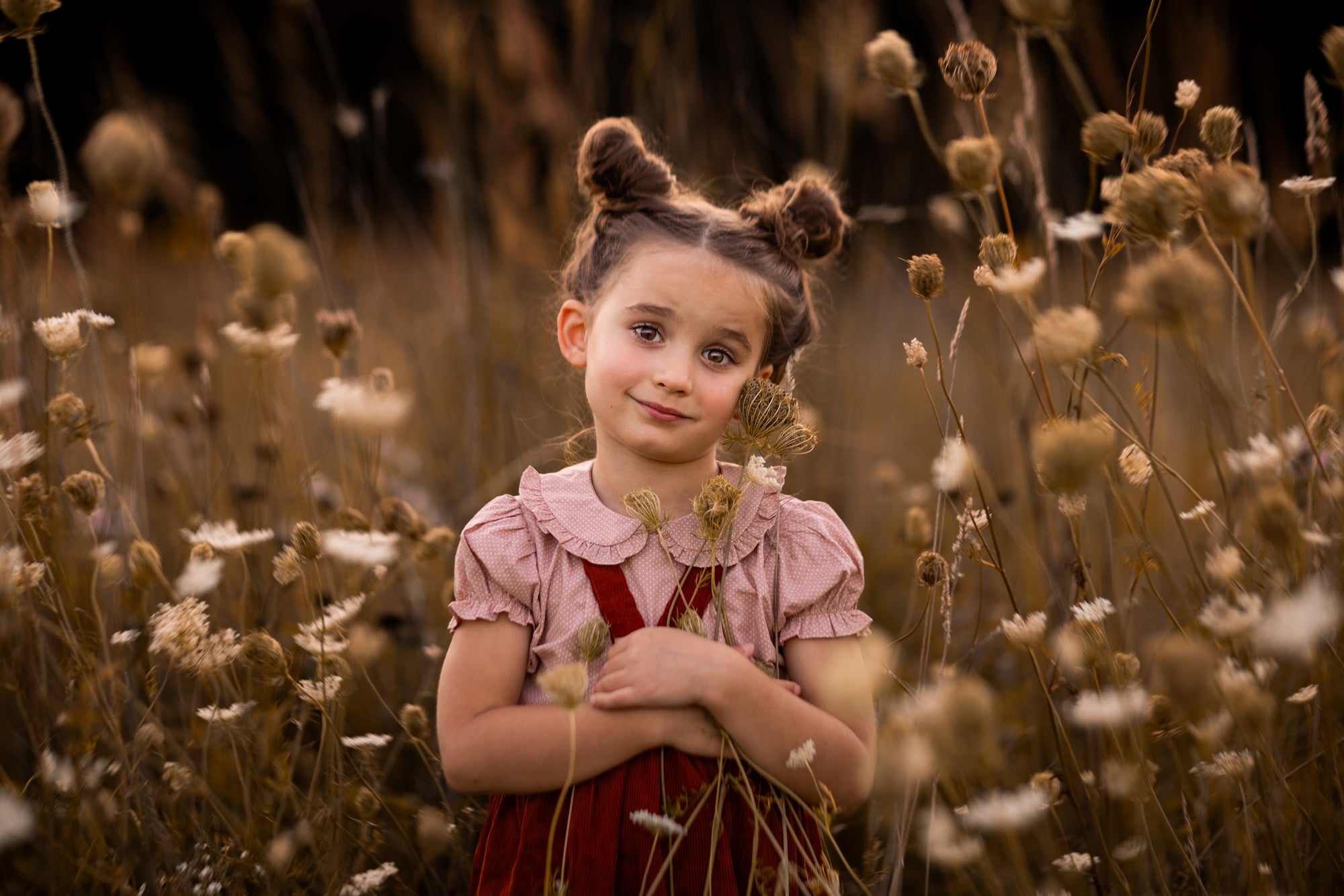 Young girl in a red dress standing among tall grass and wildflowers