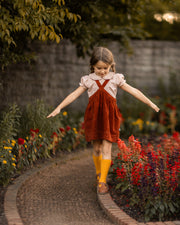 Young girl in a red dress and yellow socks standing on a garden path with flowers around.