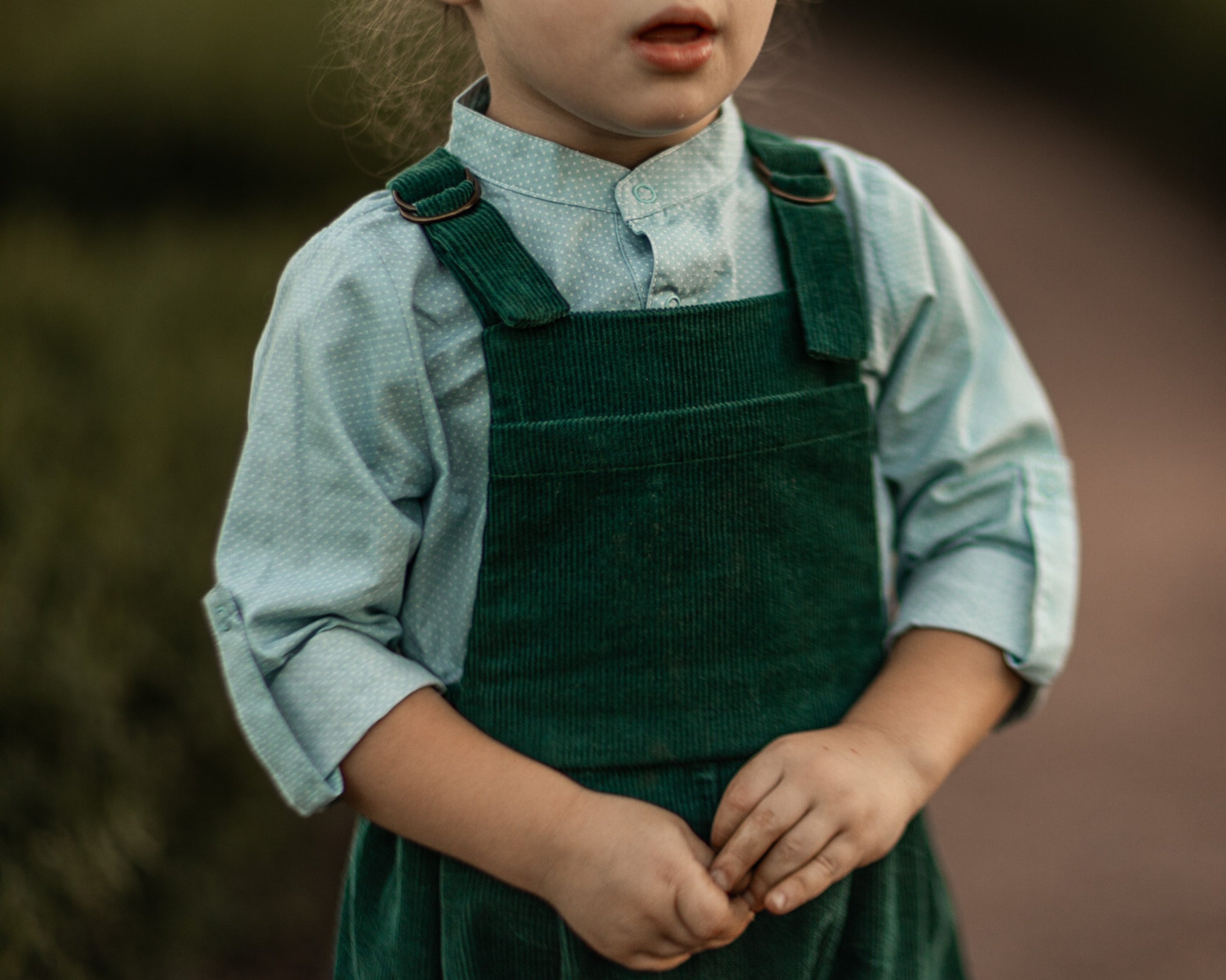 A 3-year-old model boy showcasing a classic light blue Henley shirt with white Swiss dots, crafted from natural, sustainable, and high-quality materials. He pairs it with spruce corduroy long overalls, which add a rich texture and warmth to the outfit. The combination highlights the playful yet stylish nature of children's fashion, perfect for both casual outings and special occasions.
