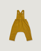 A mustard yellow baby romper with shoulder straps that cross over at the back, an elastic waistband, and wide legs with rolled cuffs, shown flat on a light gray background.
