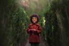 Child in a red coat standing between two tall green bushes