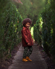 Child in a red coat standing in a garden path lined with green hedges