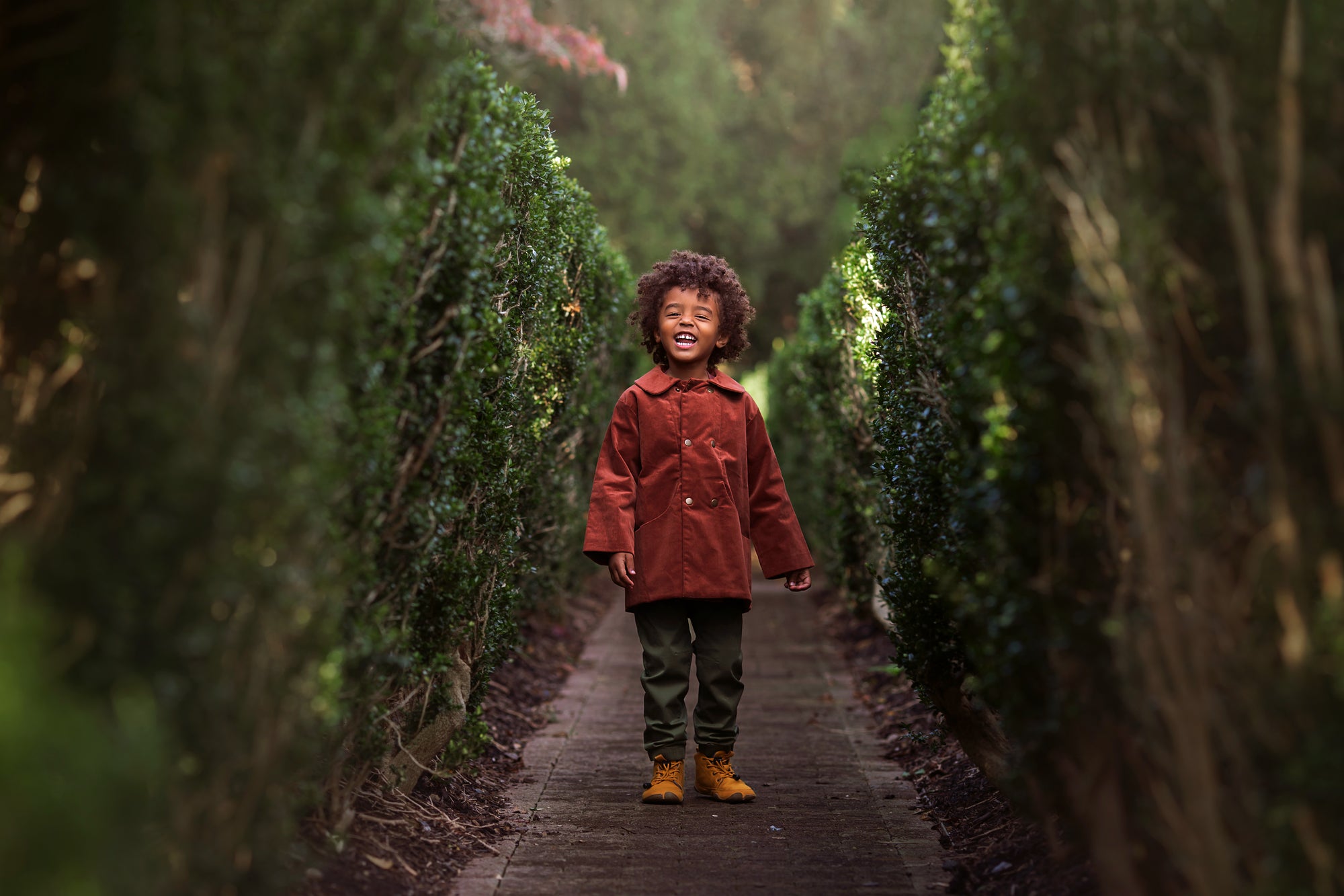 Child in a red coat standing between two rows of trimmed hedges