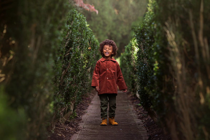 Child in a red coat standing between two rows of trimmed hedges