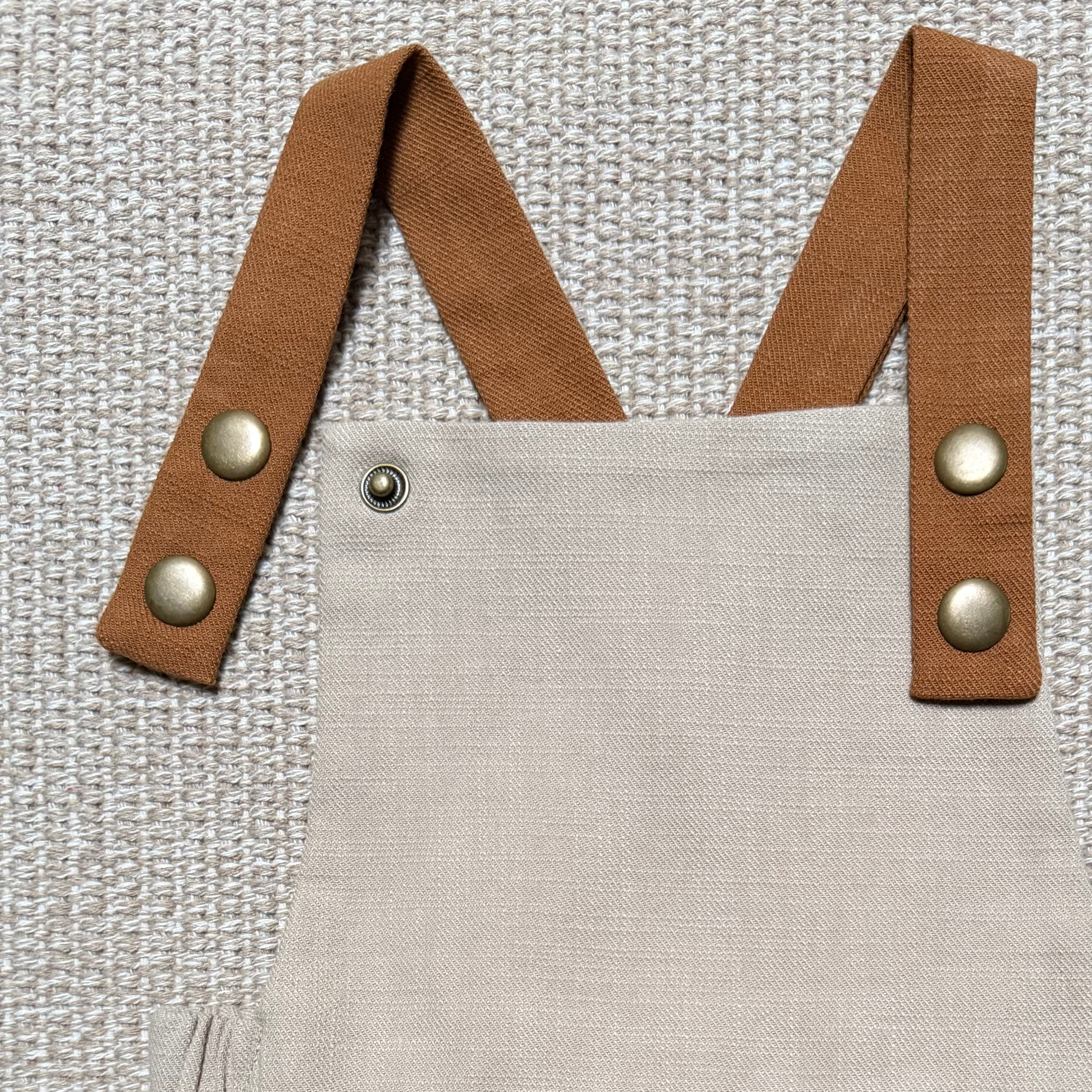 Beige overalls with brown straps and buttons on a textured gray background