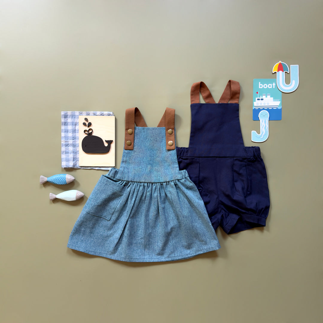 Children's denim dress with brown straps and navy shorts on a beige background