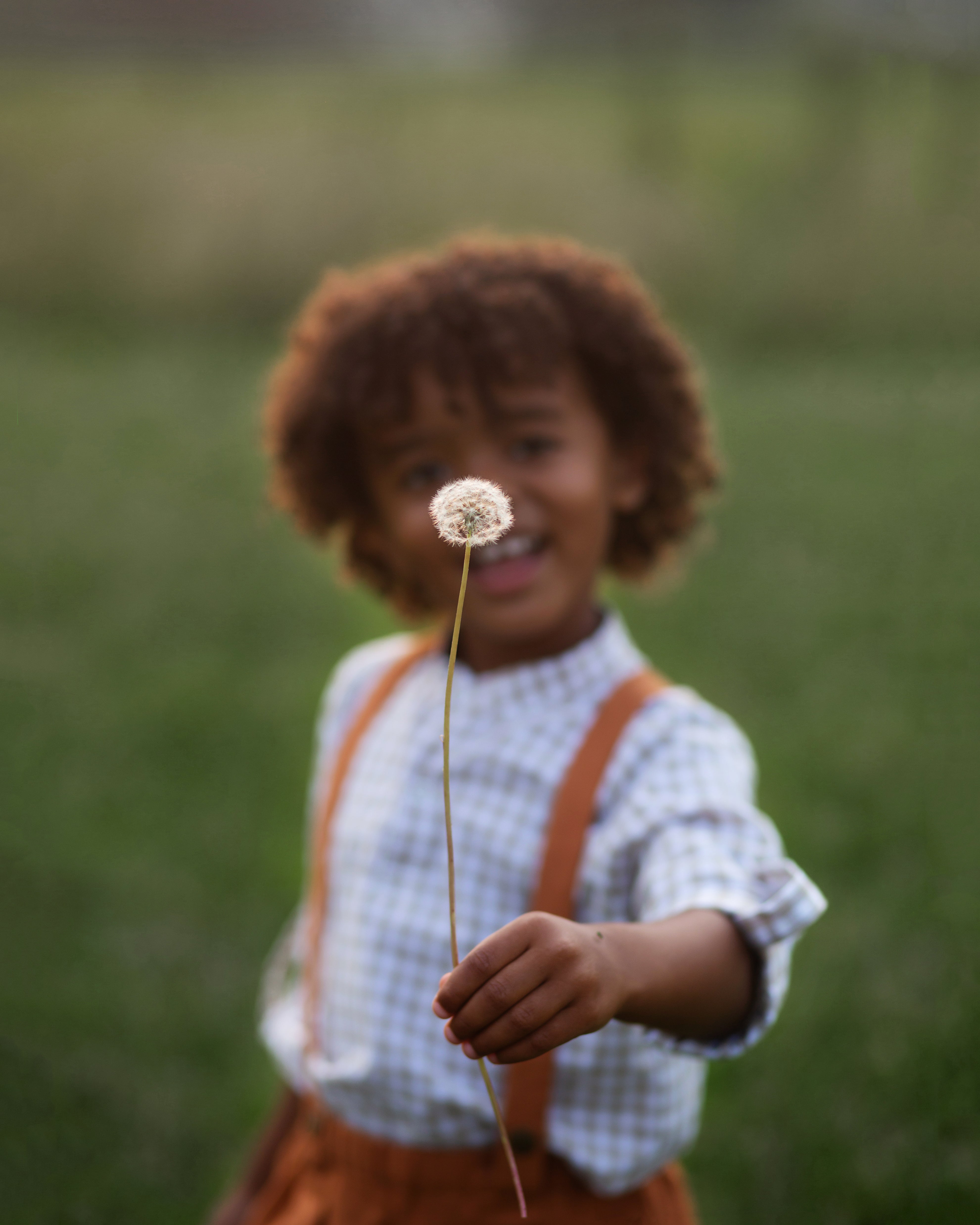 Playful image of Beige Gingham Henley Shirt worn by 5-year-old boy in size 5Y, featuring a classic Henley placket and 3/4 cuffed sleeves that can be unrolled for layering. Paired with burnt orange linen suspender shorts for a stylish, versatile outfit.