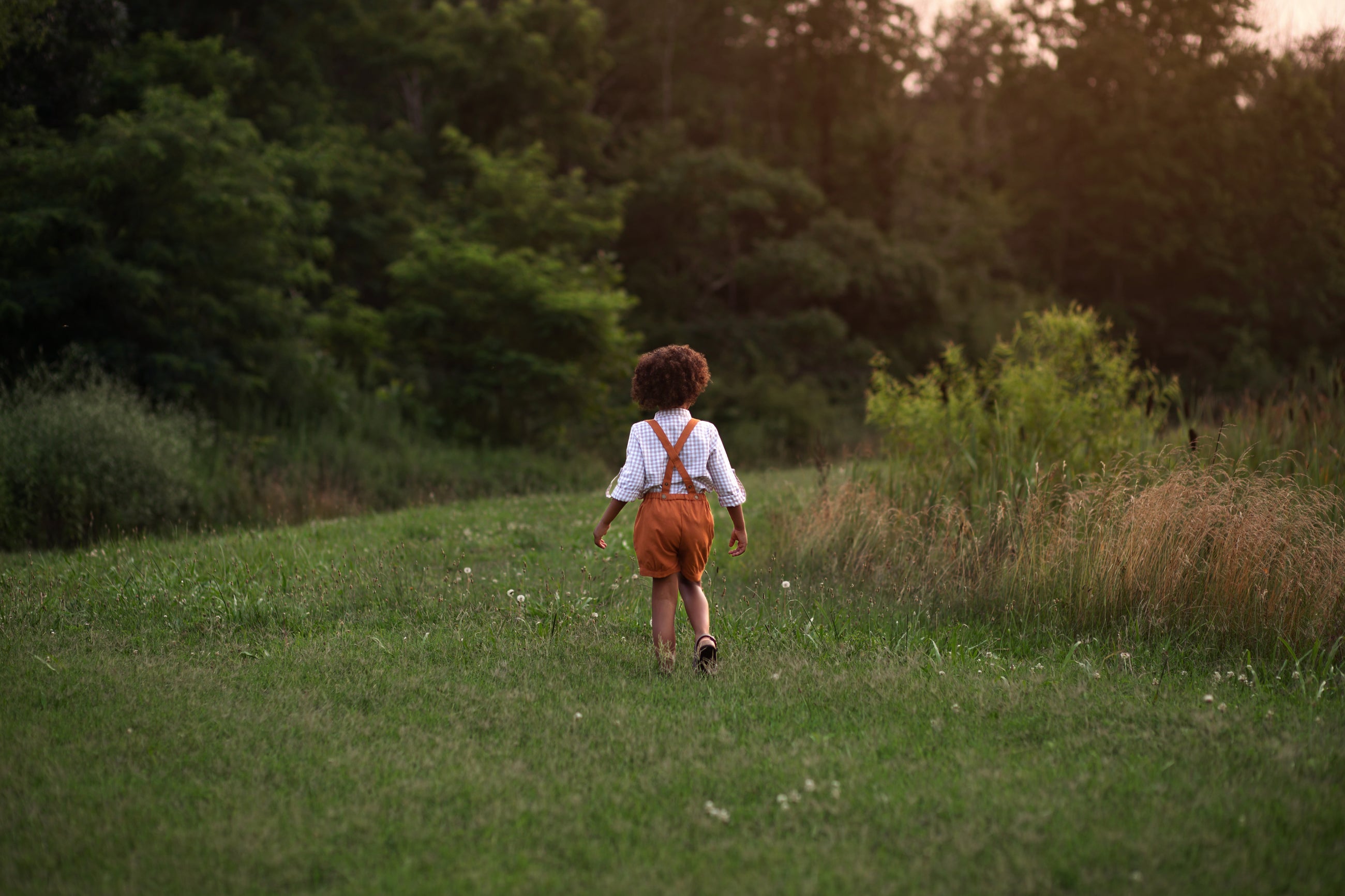 Model boy wearing the Burnt Orange Suspender Shorts with Beige Gingham Henley Shirt, back view - This image showcases the back of the outfit, highlighting the adjustable straps and how they complement the overall look.