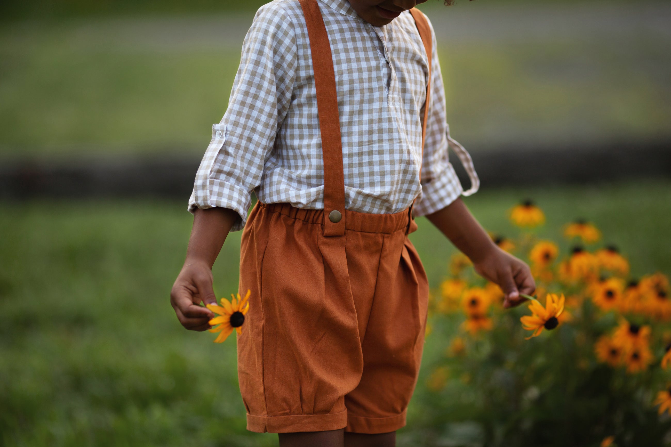 Model boy wearing the Burnt Orange Suspender Shorts with Beige Gingham Henley Shirt, detail view - A close-up shot focusing on the pleats and cuffs of the shorts, emphasizing the quality craftsmanship and design elements.