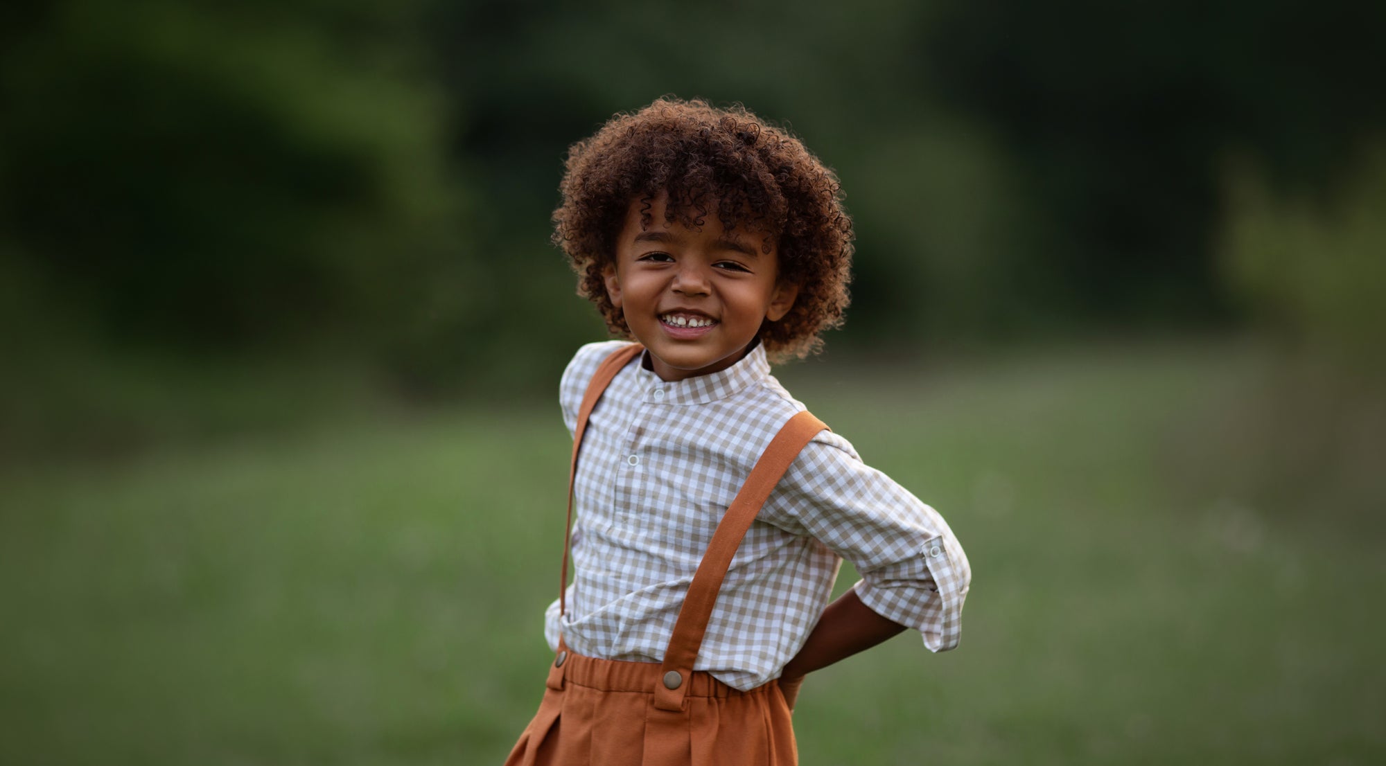 Beige Gingham Henley Shirt worn by a laughing 5-year-old boy in size 5Y, featuring a classic Henley placket and 3/4 cuffed sleeves that can be unrolled for layering. Paired with burnt orange linen suspender shorts for a stylish, versatile outfit.