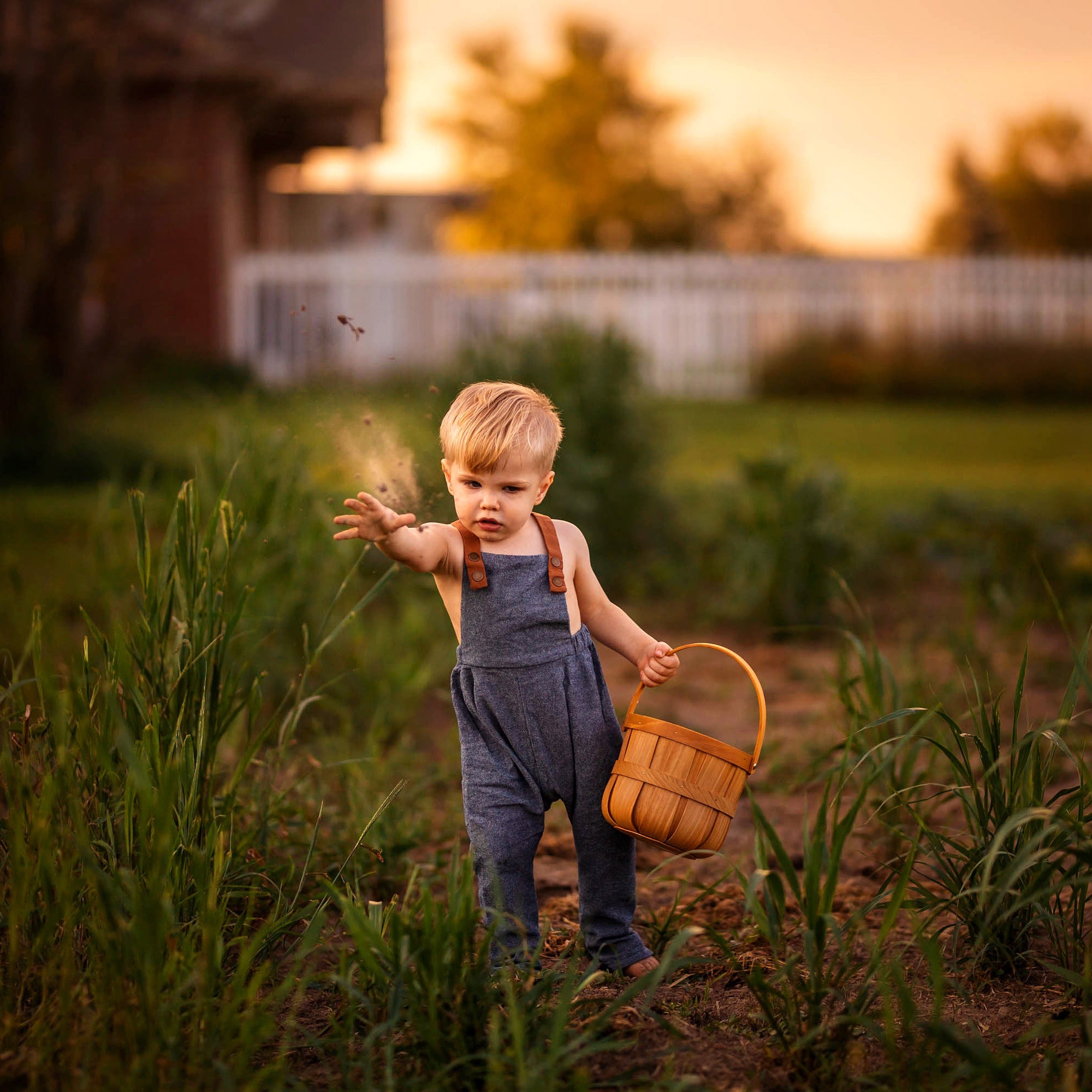 Chambray blue long overalls on a little boy model playing with soil in the summer - Handmade from repurposed linen fabric, these gender-neutral overalls are perfect for passing down. The breathable fabric ensures comfort during summer play, while stylish pleats add a touch of elegance. Featuring durable leather-looking straps, adjustable straps in two lengths provide a great fit, and unfoldable leg cuffs designed to grow with your little one make these overalls a versatile and sustainable choice for active 