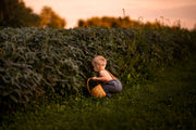 Model Squatting by Cornfield in Chambray Blue Linen Long Overalls: The model is captured squatting comfortably by a cornfield in the Chambray Blue Long Overalls, showcasing the adjustable straps for a perfect fit and the overall’s ability to keep up with little adventurers.