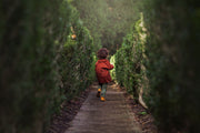 Child in a red coat walking through a tunnel of green hedges