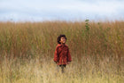 Child in a red jacket standing in tall grass with a clear sky.
