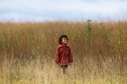 Child in a red jacket standing in tall grass with a clear sky.