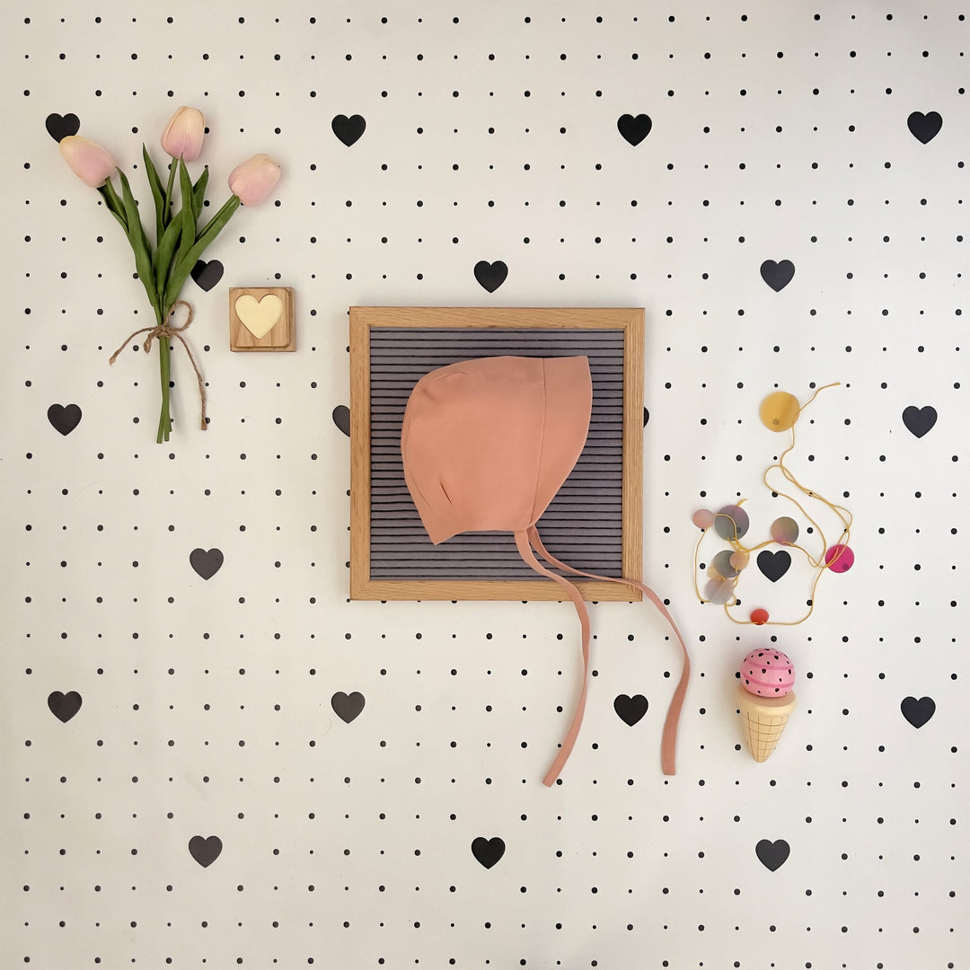 Decorative wall with a pink bonnet in a frame, tulips, and heart shapes on a pegboard.