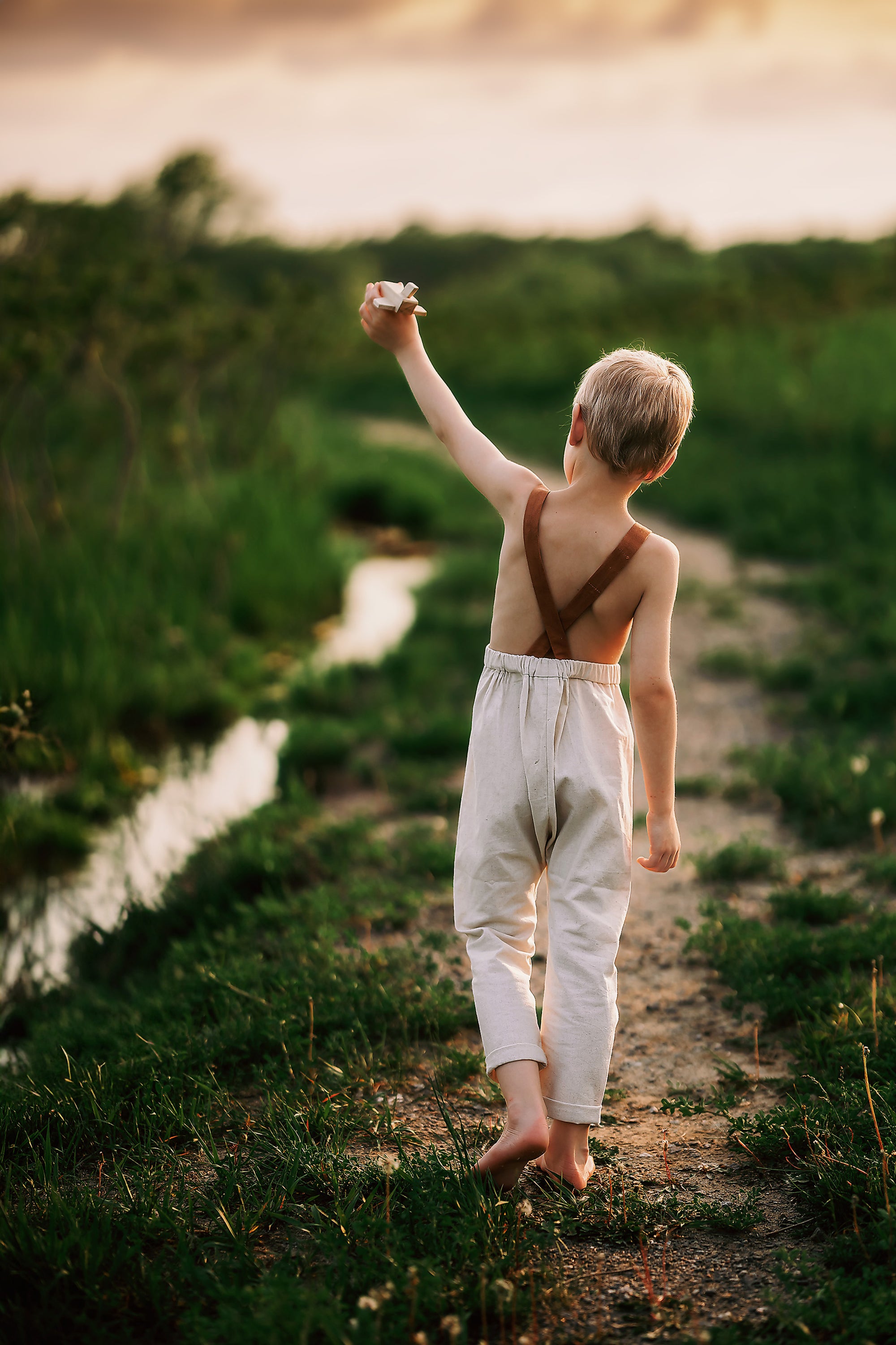 Child walking along a path by a river with a sunset in the background