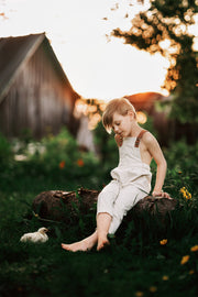 Child sitting on a log in a garden with a barn in the background