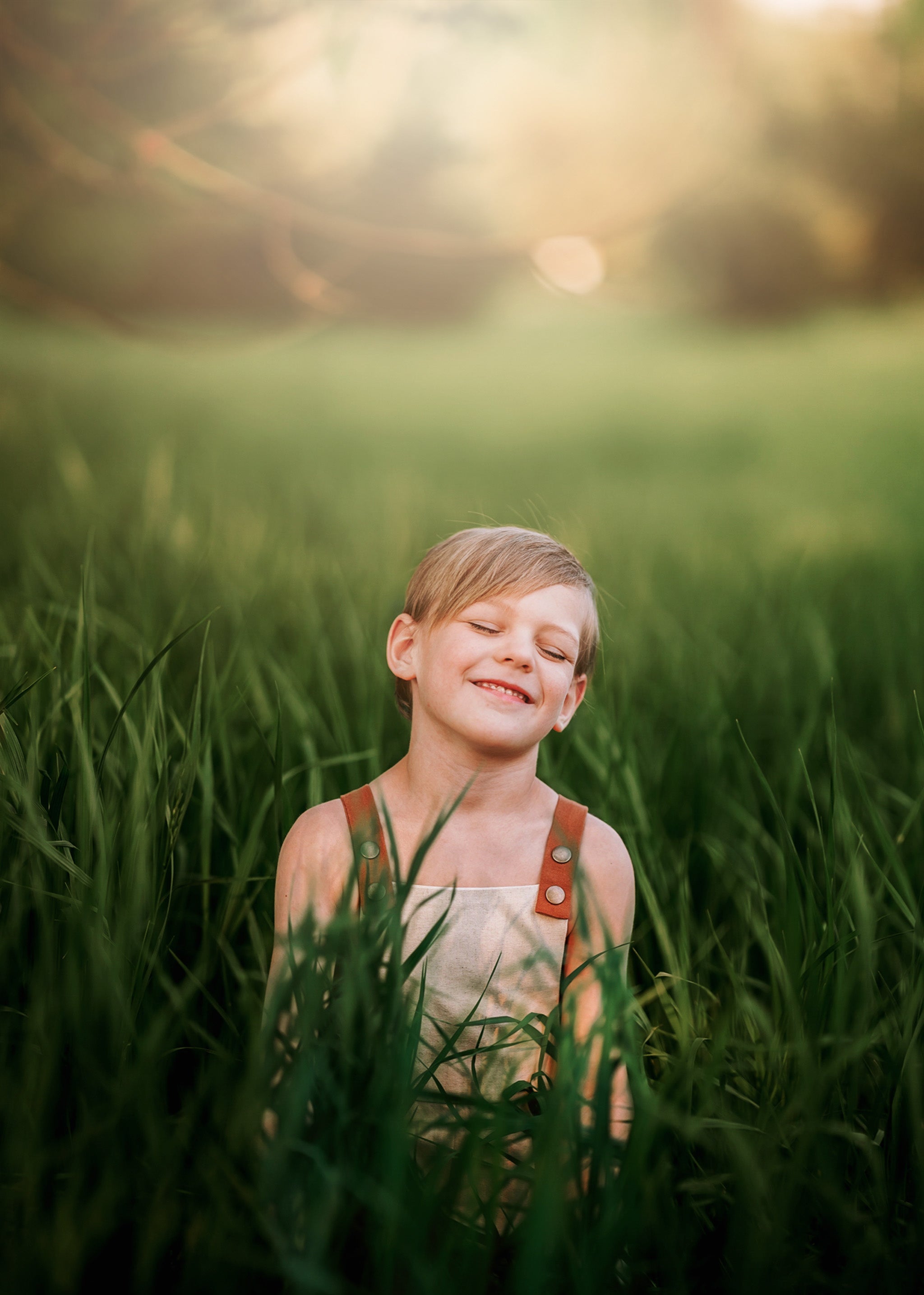 Child in overalls standing in a grassy field with a warm, blurred background