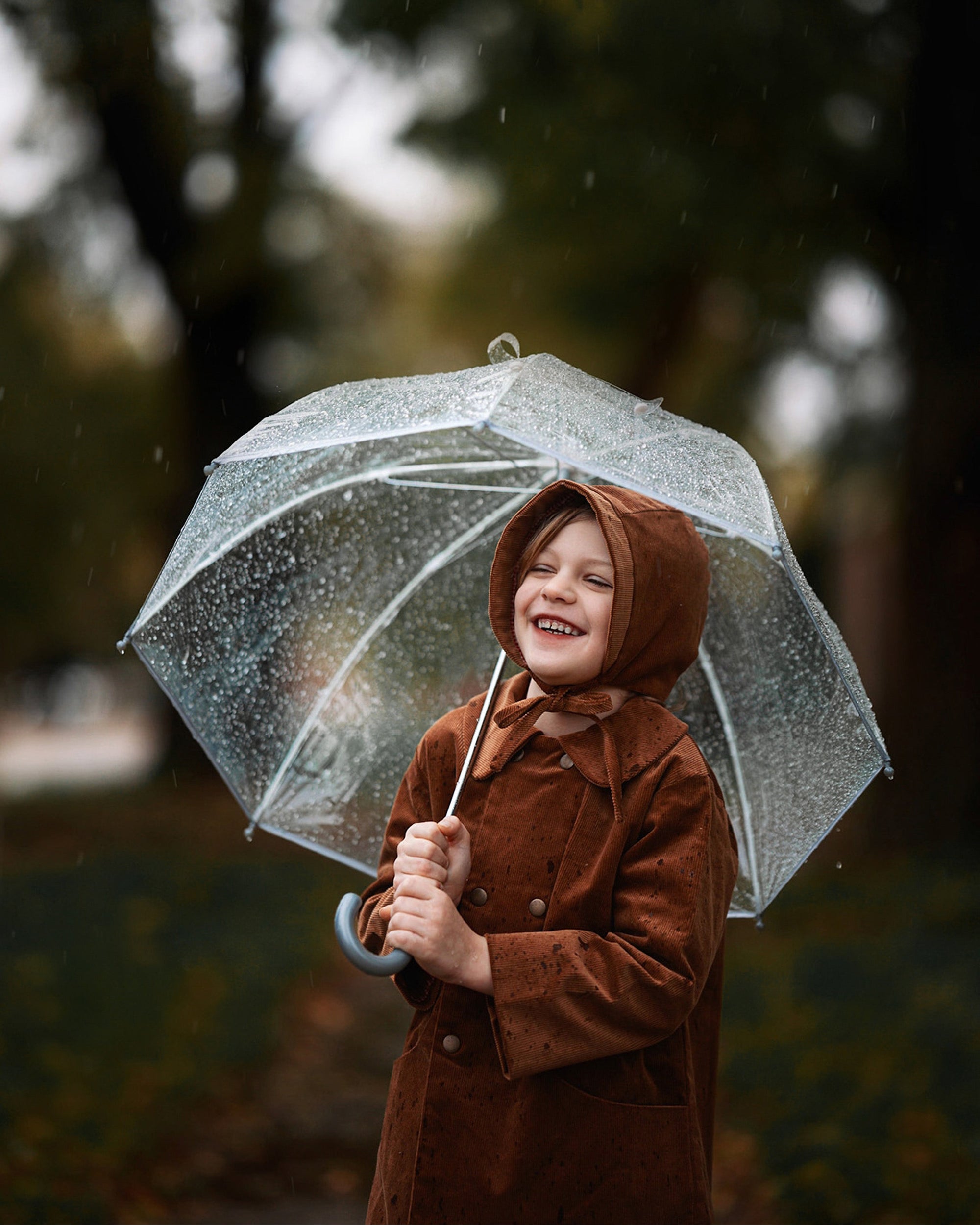 Under the Rain with Umbrella: The boy, sheltered under an umbrella, demonstrates the coat’s functionality in wet weather, looking fashionable and cozy in natural materials.