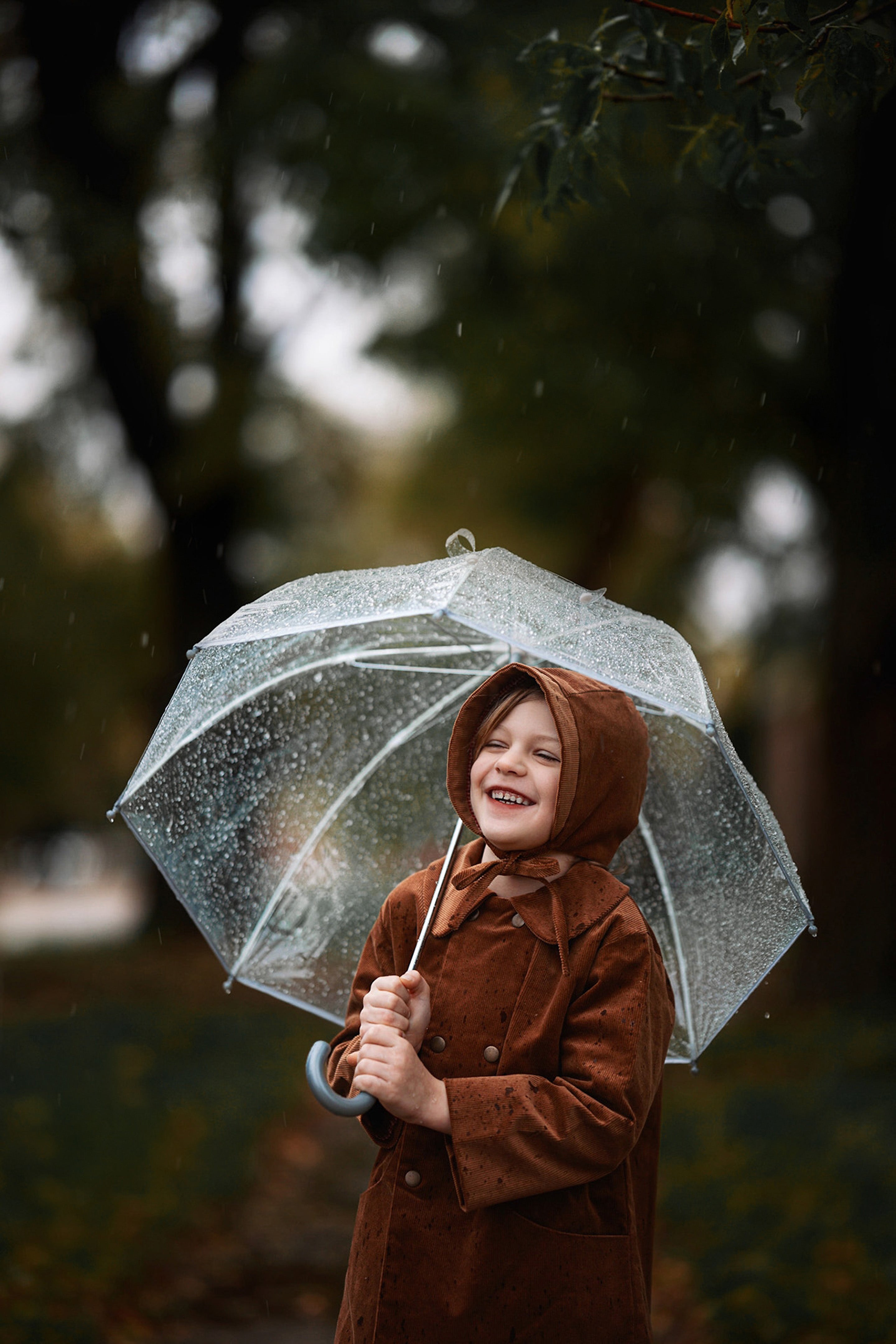 Under the Rain with Umbrella: The boy, sheltered under an umbrella, demonstrates the coat’s functionality in wet weather, looking fashionable and cozy in natural materials.