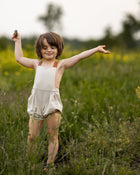 Child standing in a field with arms outstretched, holding a small object.