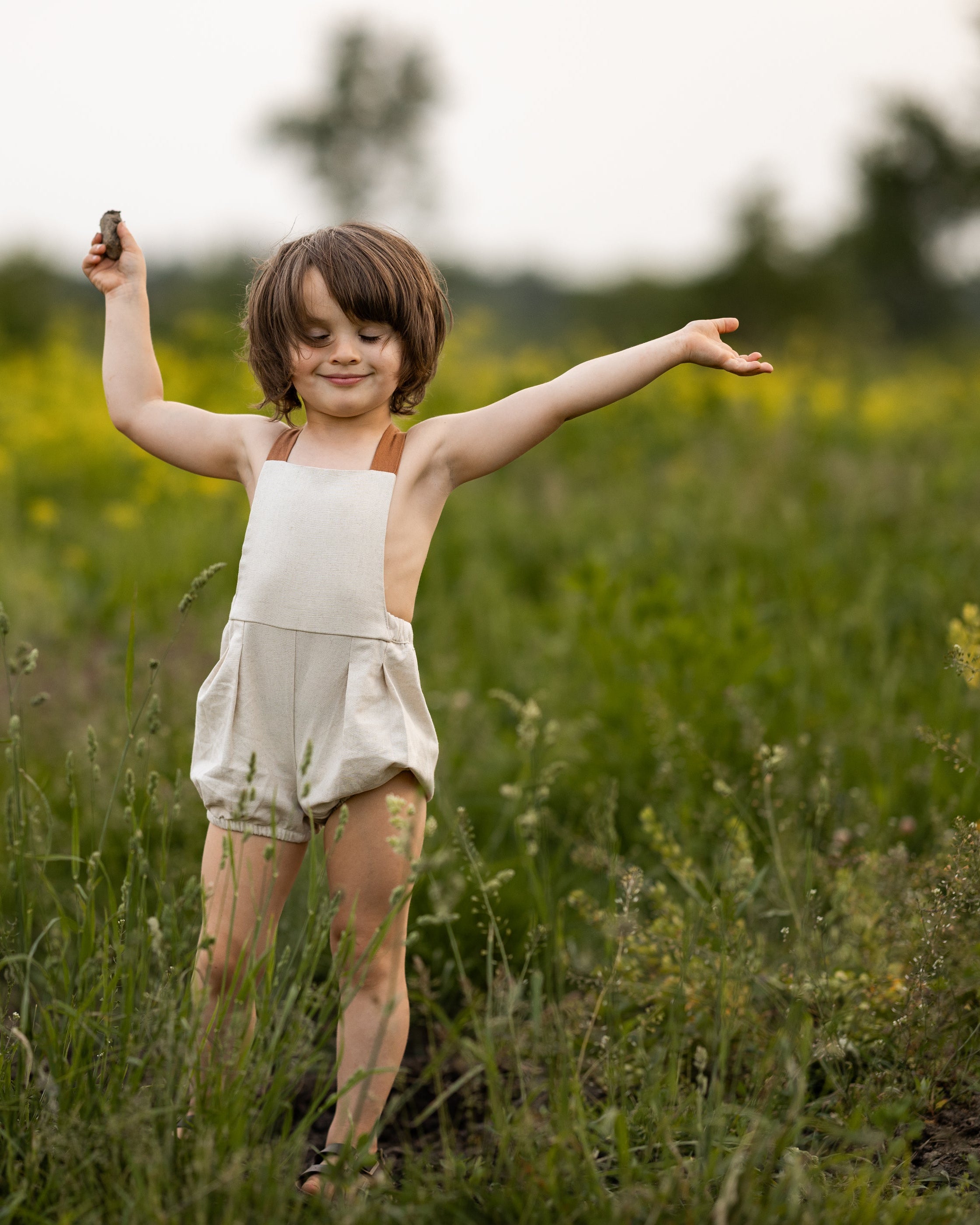 Child standing in a field with arms outstretched, holding a small object.