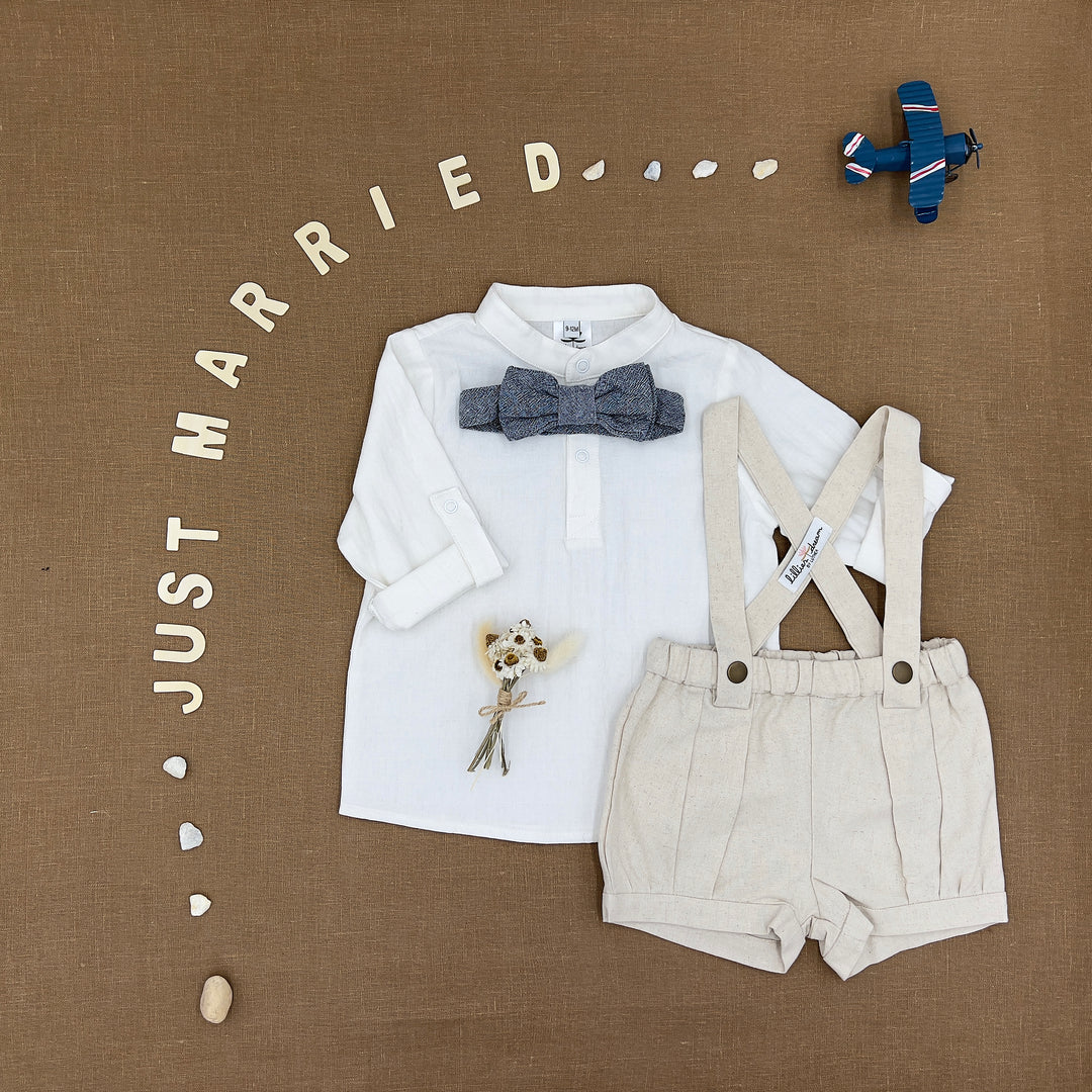 A baby boy's two-piece clothing set featuring a white long-sleeve shirt with a gray patterned bow tie and cream-colored linen suspenders, styled on a brown textured background with decorative props and 'JUST MARRIED' lettering.