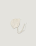 A light cream-colored linen bonnet with long ties, photographed flat on a matching light gray background.