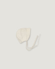 A light cream-colored linen bonnet with long ties, photographed flat on a matching light gray background.