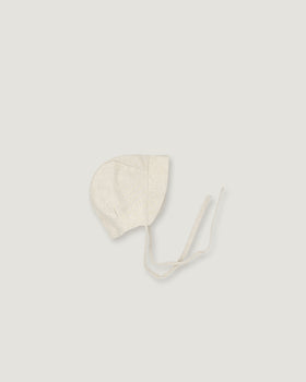 A light cream-colored linen bonnet with long ties, photographed flat on a matching light gray background.