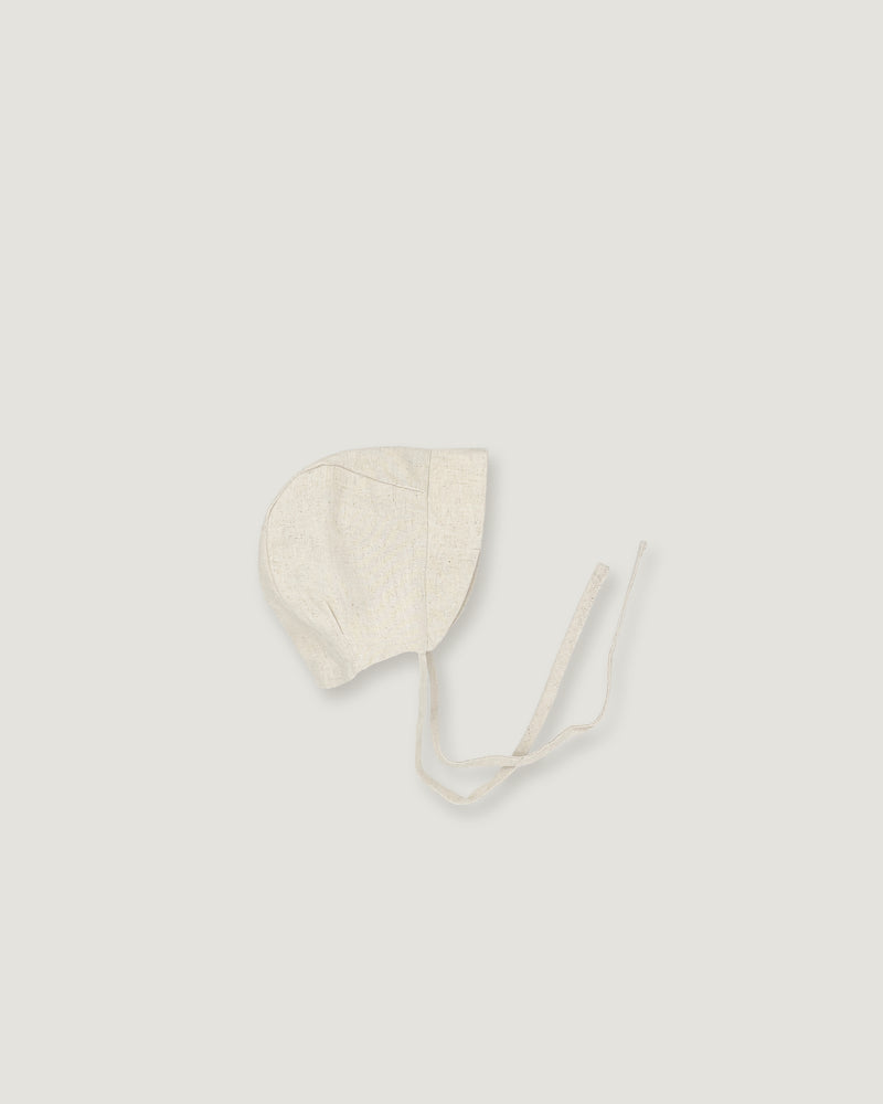 A light cream-colored linen bonnet with long ties, photographed flat on a matching light gray background.
