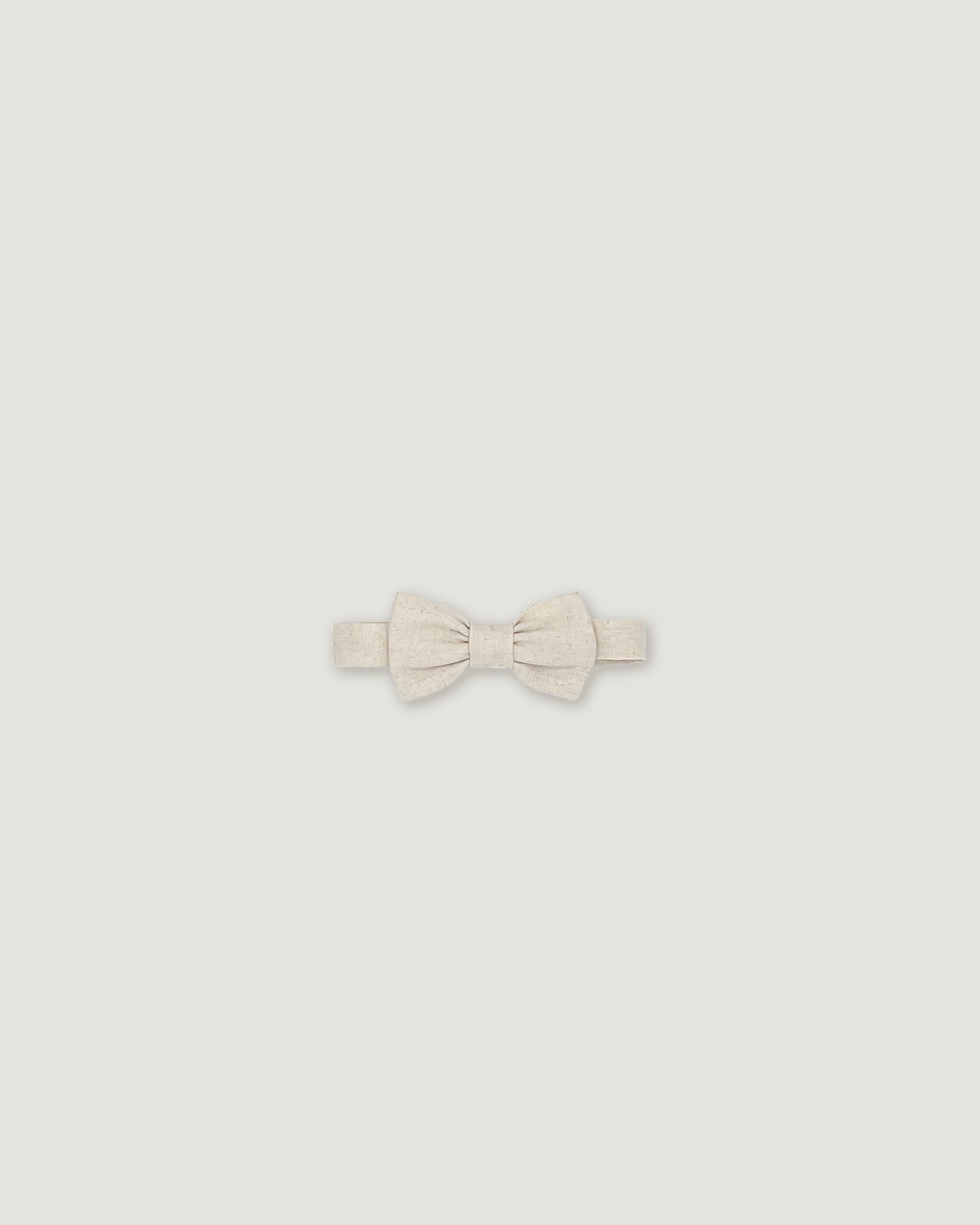 A small bowtie in a textured cream or off-white fabric, centered on a solid light gray background.