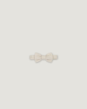 A small bowtie in a textured cream or off-white fabric, centered on a solid light gray background.