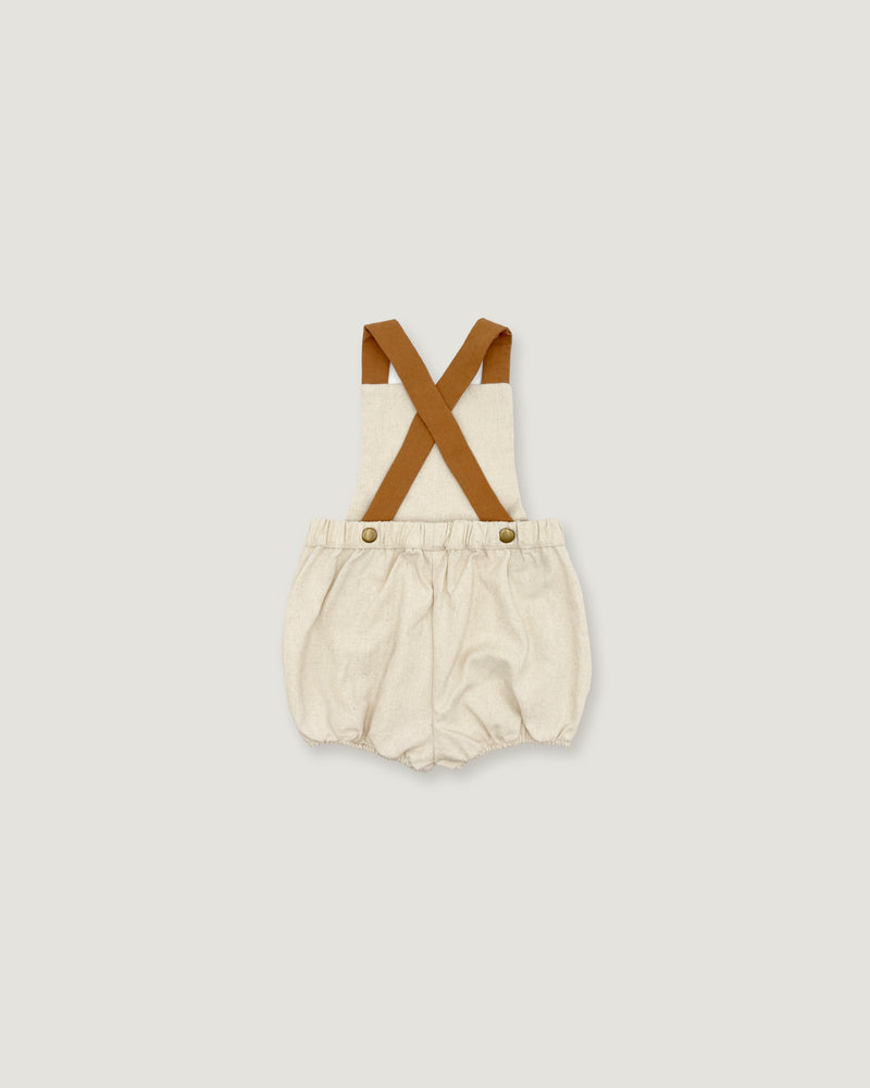 A baby romper with cream-colored fabric and brown suspenders, shown flat on a light gray background.