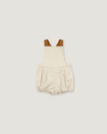 A baby romper in a textured cream linen-like fabric, featuring brown shoulder straps, displayed flat against a solid light gray background.
