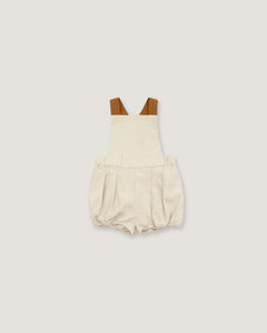 A baby romper in a textured cream linen-like fabric, featuring brown shoulder straps, displayed flat against a solid light gray background.