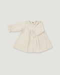 A light beige linen long-sleeve dress for toddlers, featuring a gathered waist with a bow detail, pleated front, and elasticized cuffs, shown on a neutral light gray background.