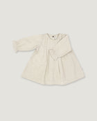 A light beige linen long-sleeve dress for toddlers, featuring a gathered waist with a bow detail, pleated front, and elasticized cuffs, shown on a neutral light gray background.