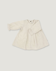 A light beige linen long-sleeve dress for toddlers, featuring a gathered waist with a bow detail, pleated front, and elasticized cuffs, shown on a neutral light gray background.