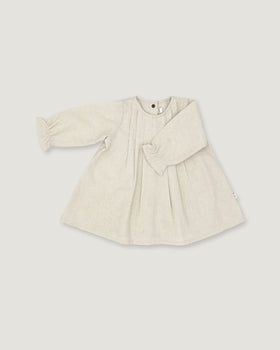 A light beige linen long-sleeve dress for toddlers, featuring a gathered waist with a bow detail, pleated front, and elasticized cuffs, shown on a neutral light gray background.