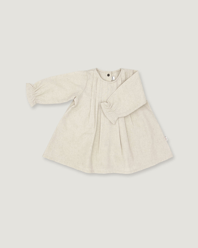 A light beige linen long-sleeve dress for toddlers, featuring a gathered waist with a bow detail, pleated front, and elasticized cuffs, shown on a neutral light gray background.