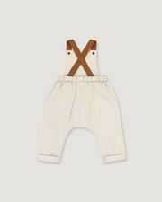 A pair of baby bib pants in a light cream linen-like fabric, featuring brown faux-leather suspenders that cross over the chest. The pants have an elastic waistband and rolled cuffs, shown against a solid light gray background.