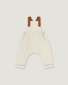 A baby romper in off-white linen with brown leather-like shoulder straps, shown flat on a light gray background.
