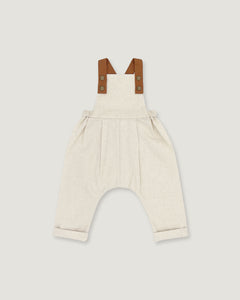 A baby romper in off-white linen with brown leather-like shoulder straps, shown flat on a light gray background.