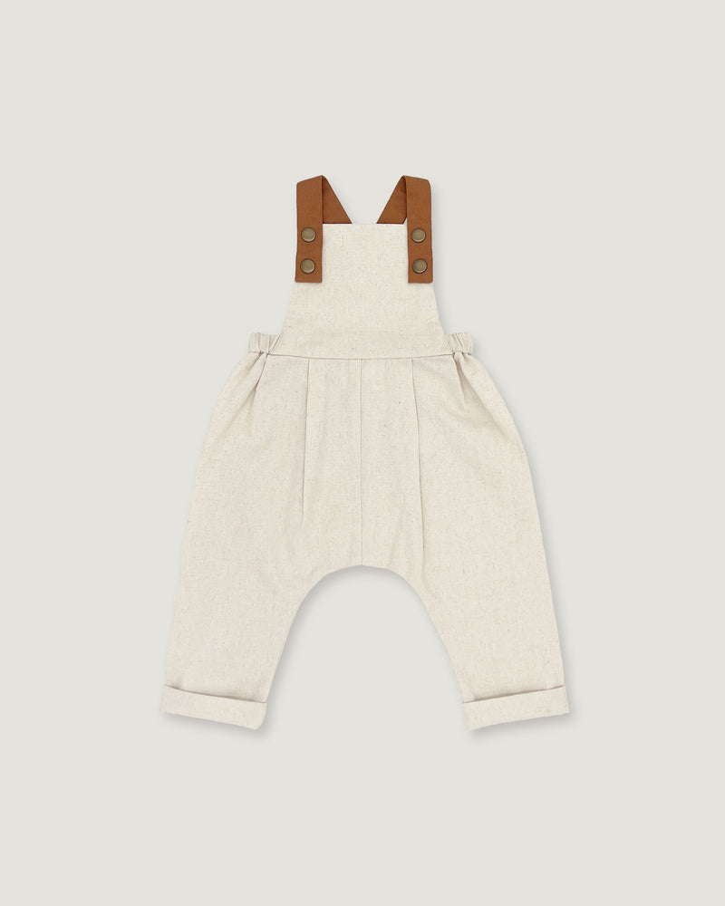 A baby romper in off-white linen with brown leather-like shoulder straps, shown flat on a light gray background.