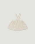 A light cream-colored linen dress with shoulder straps, laid flat against a neutral light gray background.
