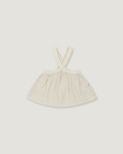 A light cream-colored linen dress with shoulder straps, laid flat against a neutral light gray background.